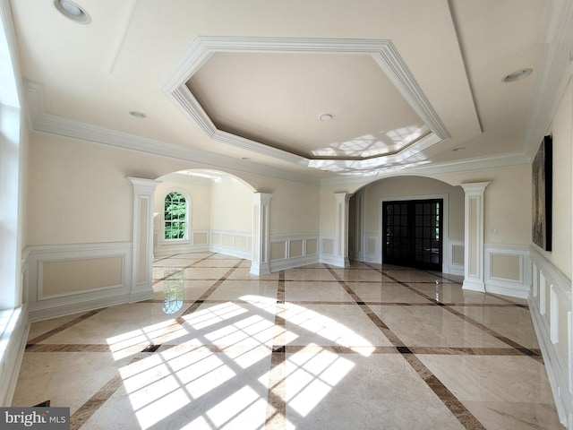 interior space featuring a tray ceiling, ornate columns, and ornamental molding