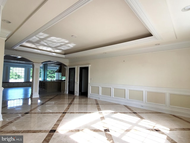 spare room with a tray ceiling, ornate columns, and crown molding