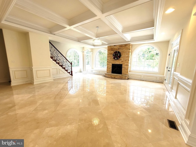 unfurnished living room with beamed ceiling, a stone fireplace, ornamental molding, and coffered ceiling