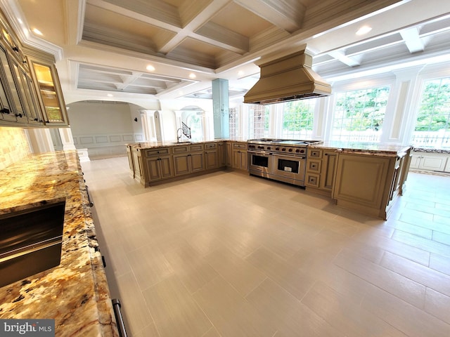 kitchen featuring coffered ceiling, light stone counters, beamed ceiling, range with two ovens, and custom exhaust hood