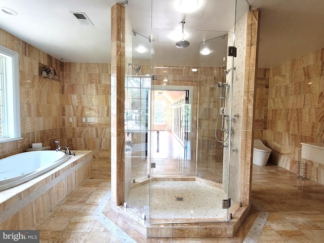 bathroom featuring separate shower and tub, toilet, and tile walls