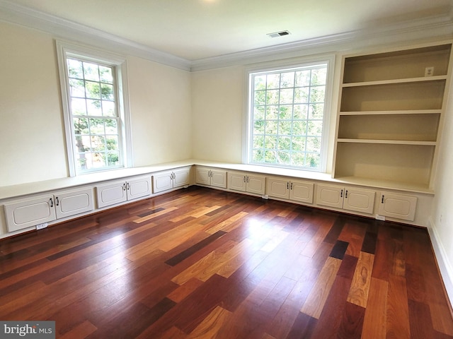 spare room with ornamental molding, built in features, plenty of natural light, and dark wood-type flooring