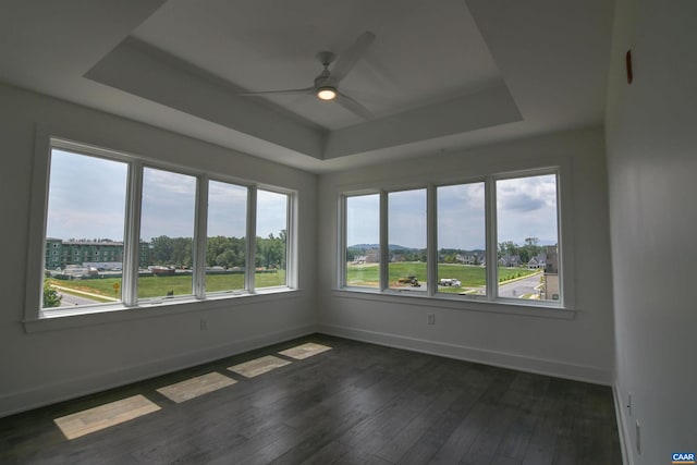 unfurnished room featuring a wealth of natural light, dark wood-type flooring, ceiling fan, and a raised ceiling