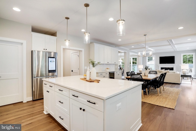 kitchen with hanging light fixtures, white cabinets, light wood-type flooring, coffered ceiling, and stainless steel fridge