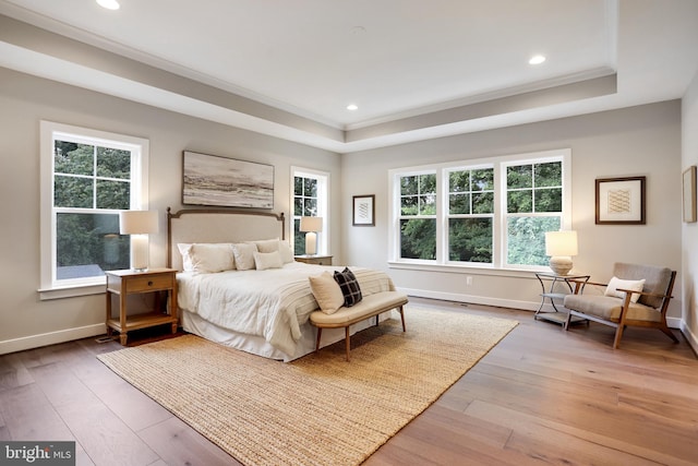 bedroom featuring wood-type flooring, multiple windows, crown molding, and a tray ceiling