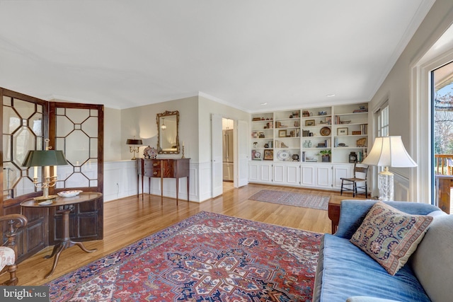 living room featuring a wainscoted wall, built in shelves, ornamental molding, and wood finished floors