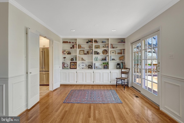 unfurnished room featuring built in shelves, wainscoting, and light wood finished floors