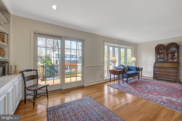 sitting room with a wainscoted wall, light wood-style flooring, visible vents, and crown molding