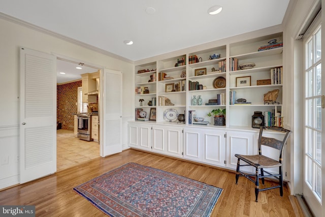 living area with built in features, crown molding, light wood-style flooring, and brick wall