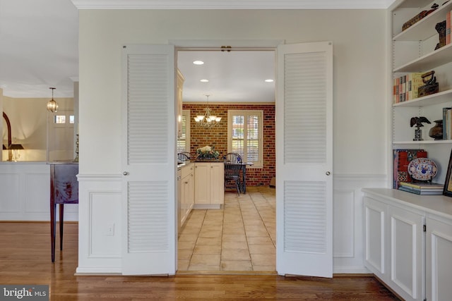 hallway featuring a chandelier, a wainscoted wall, ornamental molding, and brick wall