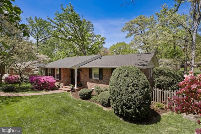 ranch-style house featuring brick siding, a front yard, fence, and a shingled roof