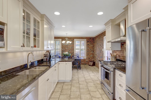 kitchen with brick wall, a sink, stainless steel appliances, wall chimney range hood, and a notable chandelier