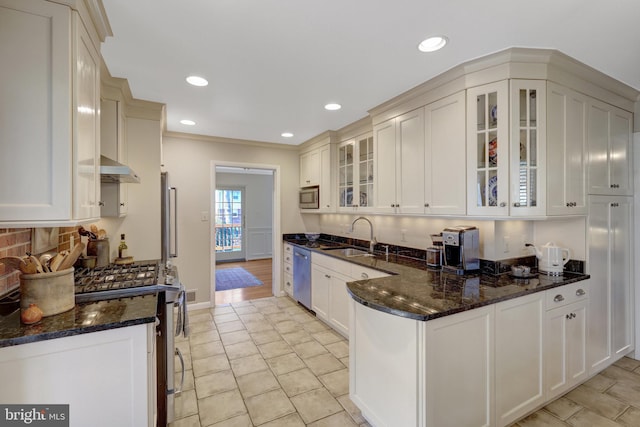 kitchen with a peninsula, a sink, appliances with stainless steel finishes, backsplash, and dark stone counters