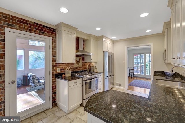 kitchen featuring dark stone countertops, a sink, stainless steel appliances, wall chimney range hood, and backsplash