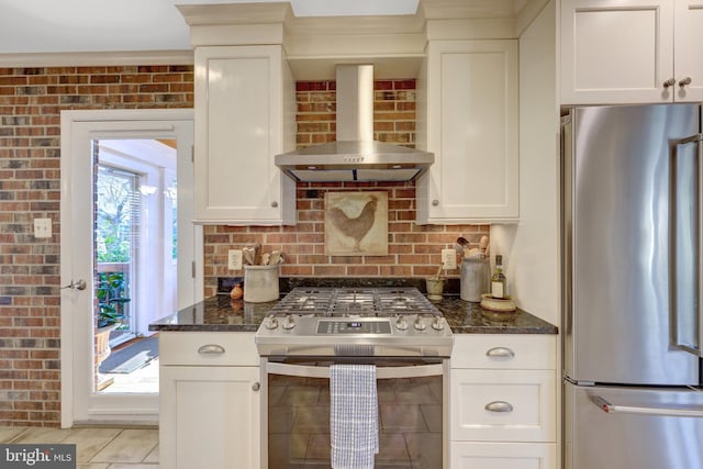 kitchen featuring brick wall, wall chimney exhaust hood, stainless steel appliances, and backsplash