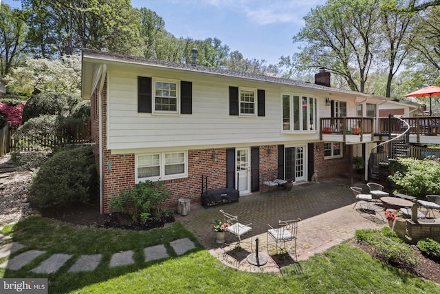 view of front facade featuring brick siding, a patio, a chimney, a deck, and stairs