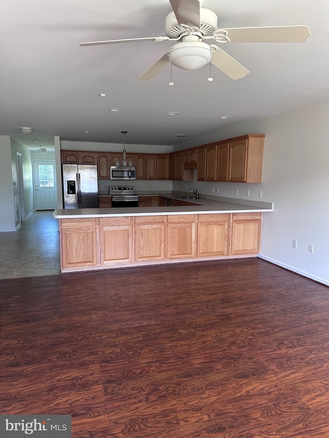 kitchen featuring kitchen peninsula, pendant lighting, stainless steel appliances, and dark wood-type flooring