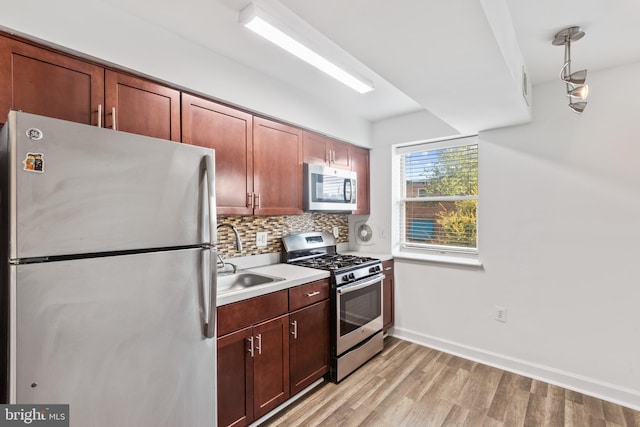 kitchen featuring decorative backsplash, light wood-type flooring, stainless steel appliances, sink, and pendant lighting