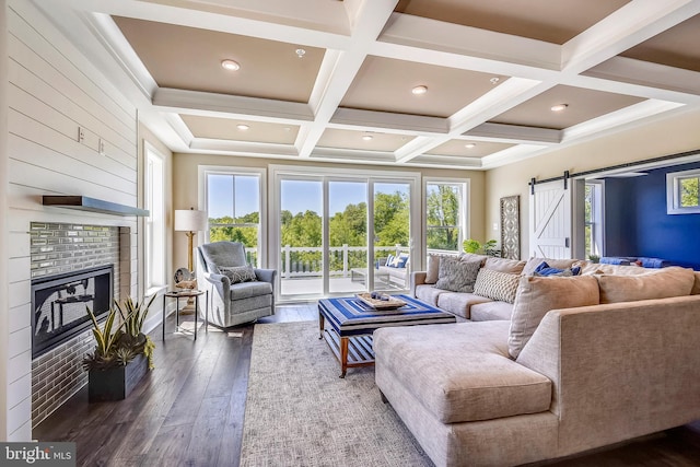 living room featuring a barn door, beam ceiling, coffered ceiling, a fireplace, and dark hardwood / wood-style flooring