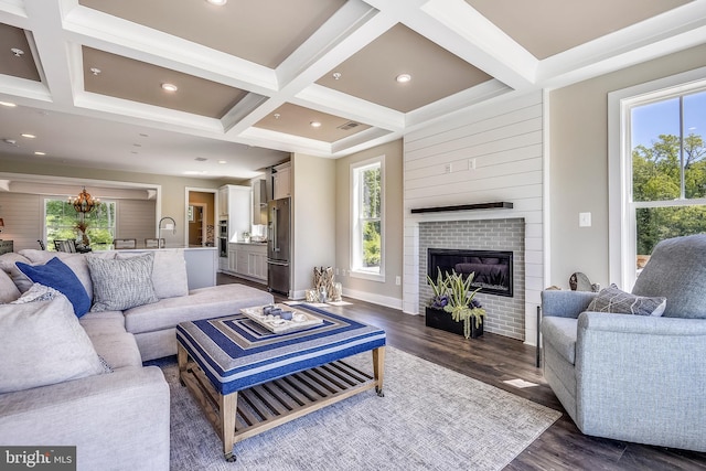 living room with beamed ceiling, a brick fireplace, coffered ceiling, sink, and dark hardwood / wood-style floors