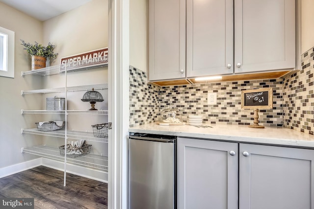 kitchen with refrigerator, gray cabinets, dark wood-type flooring, backsplash, and light stone counters