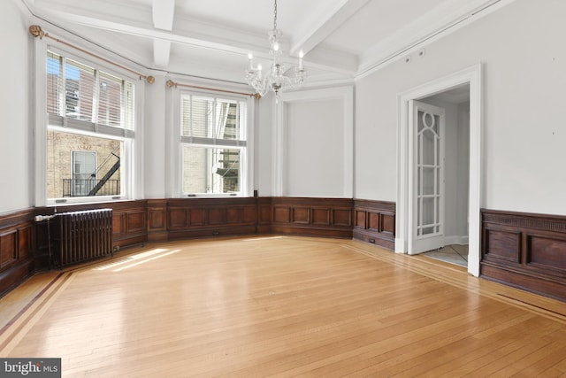 empty room with beamed ceiling, light hardwood / wood-style flooring, radiator, and an inviting chandelier