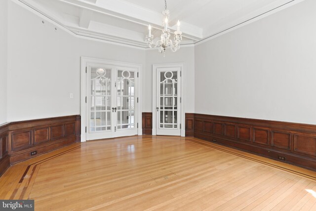 empty room with coffered ceiling, a notable chandelier, beam ceiling, french doors, and light hardwood / wood-style flooring