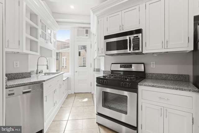 kitchen featuring appliances with stainless steel finishes, light tile flooring, a wall unit AC, white cabinetry, and sink