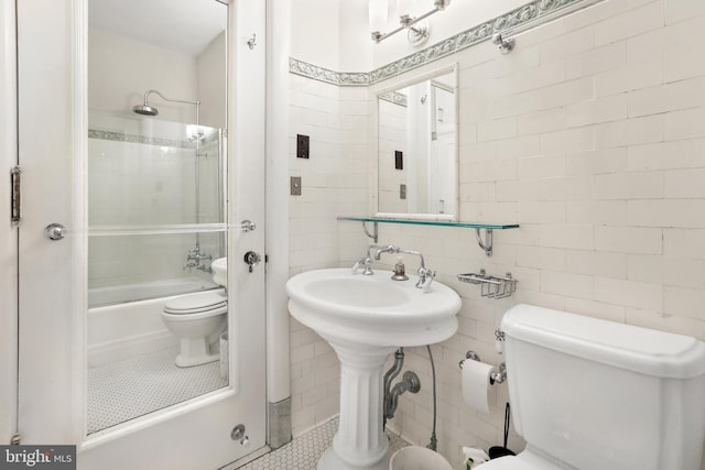 bathroom featuring tile flooring, tile walls, toilet, and bath / shower combo with glass door