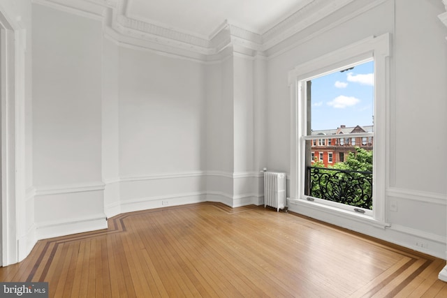 spare room featuring a healthy amount of sunlight, light hardwood / wood-style flooring, ornamental molding, and radiator heating unit