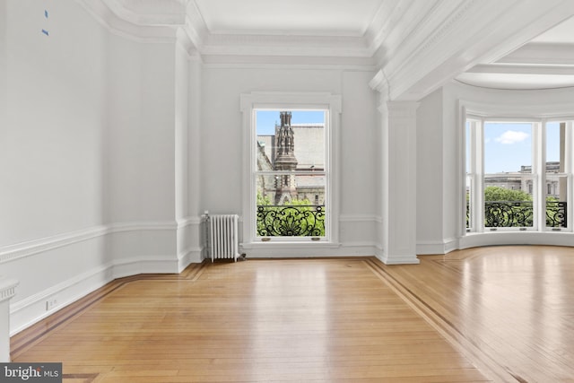 interior space with ornamental molding, light wood-type flooring, decorative columns, and radiator heating unit