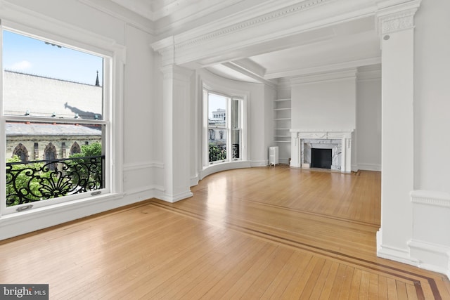 unfurnished living room with ornamental molding, built in features, light wood-type flooring, and a premium fireplace