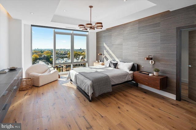 bedroom featuring a chandelier, wood-type flooring, a wall of windows, and a tray ceiling