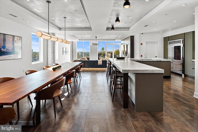 kitchen with hanging light fixtures, a large island with sink, wall oven, a tray ceiling, and a breakfast bar area