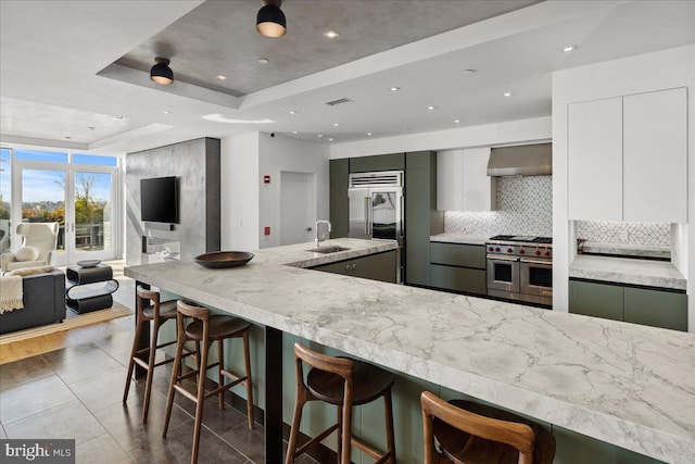 kitchen featuring wall chimney exhaust hood, light hardwood / wood-style floors, high quality appliances, backsplash, and a raised ceiling