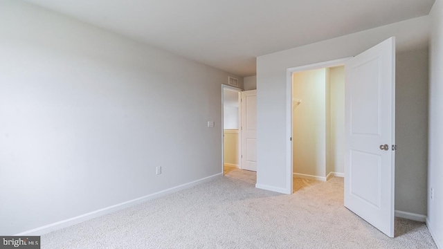 unfurnished bedroom featuring a walk in closet, light carpet, and a closet