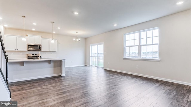 kitchen with dark wood-type flooring, hanging light fixtures, stainless steel appliances, and a center island with sink