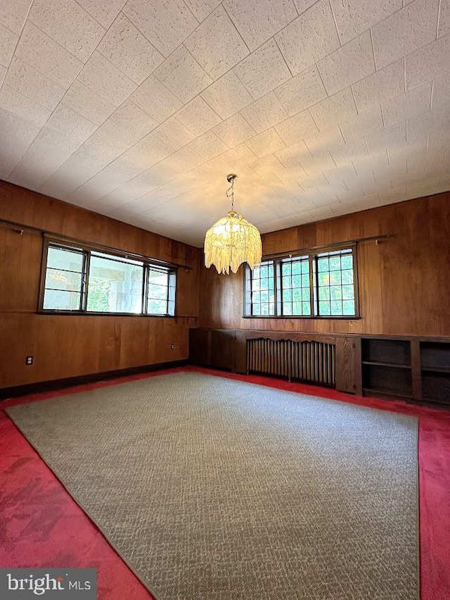 carpeted empty room featuring a notable chandelier, wood walls, and radiator