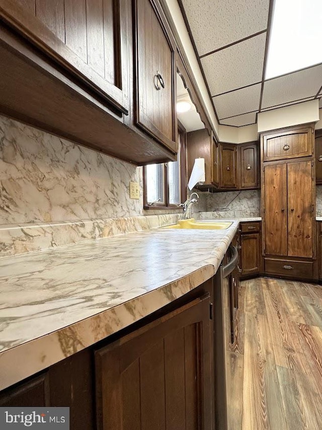 kitchen featuring sink, a drop ceiling, tasteful backsplash, dark brown cabinets, and light hardwood / wood-style flooring