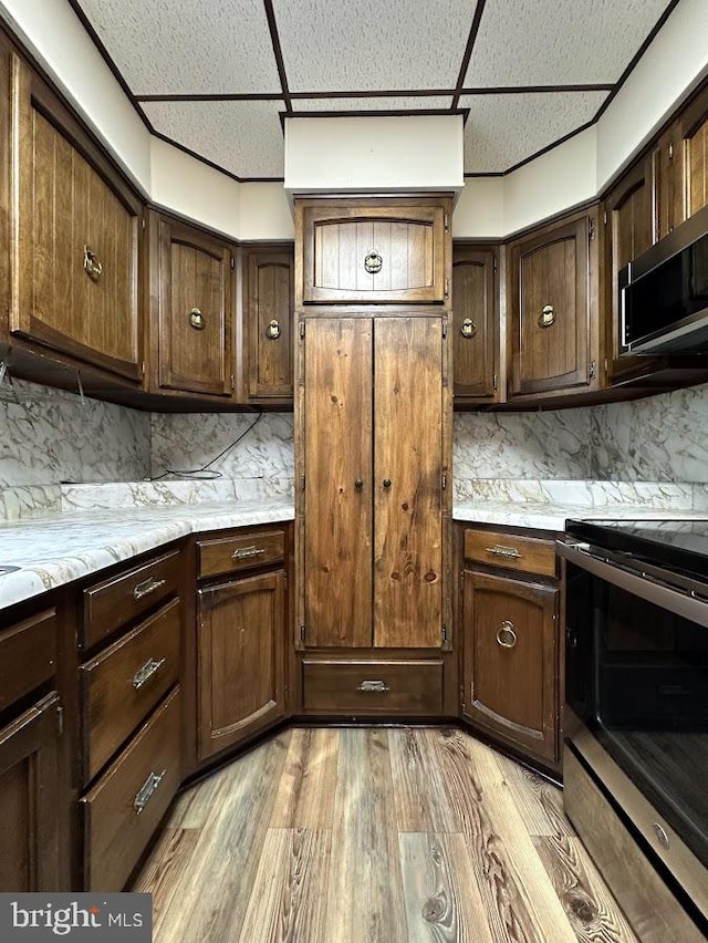 kitchen with a drop ceiling, backsplash, appliances with stainless steel finishes, dark brown cabinetry, and light wood-type flooring