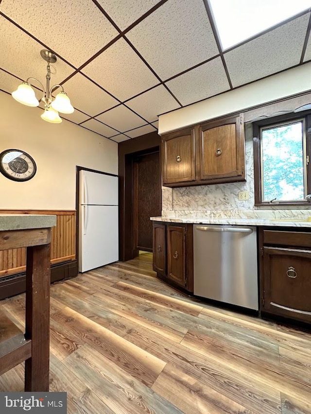 kitchen featuring a paneled ceiling, light wood-type flooring, stainless steel dishwasher, white refrigerator, and decorative light fixtures