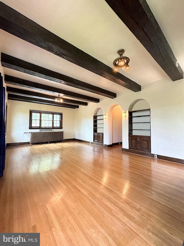 unfurnished living room with beamed ceiling, hardwood / wood-style floors, radiator heating unit, and built in shelves