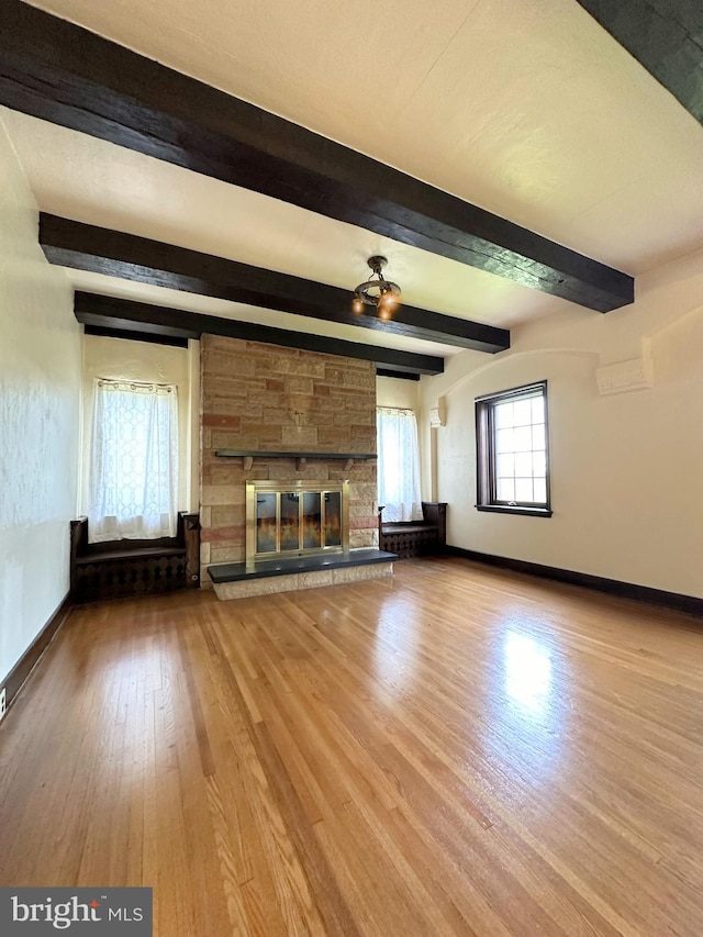 unfurnished living room with a stone fireplace, wood-type flooring, and beamed ceiling