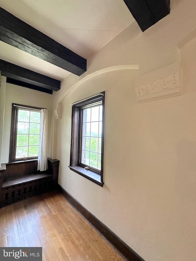 unfurnished room featuring a healthy amount of sunlight, beamed ceiling, and hardwood / wood-style floors