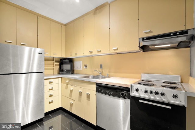 kitchen with appliances with stainless steel finishes, cream cabinetry, sink, and dark tile floors