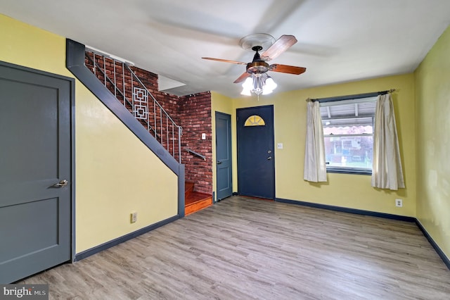 foyer entrance with brick wall, wood-type flooring, and ceiling fan