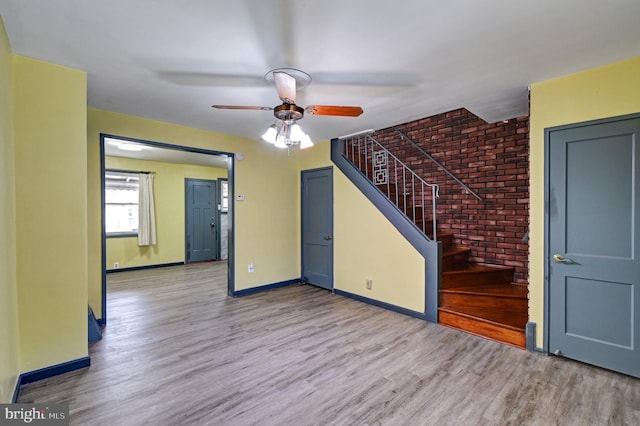 empty room featuring brick wall, ceiling fan, and light wood-type flooring