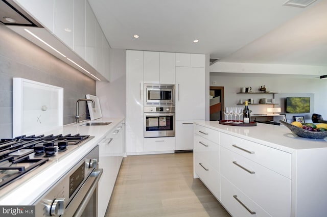 kitchen with light wood-type flooring, white cabinetry, appliances with stainless steel finishes, sink, and tasteful backsplash