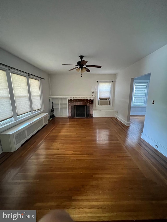 unfurnished living room with a brick fireplace, dark hardwood / wood-style floors, ceiling fan, and radiator heating unit