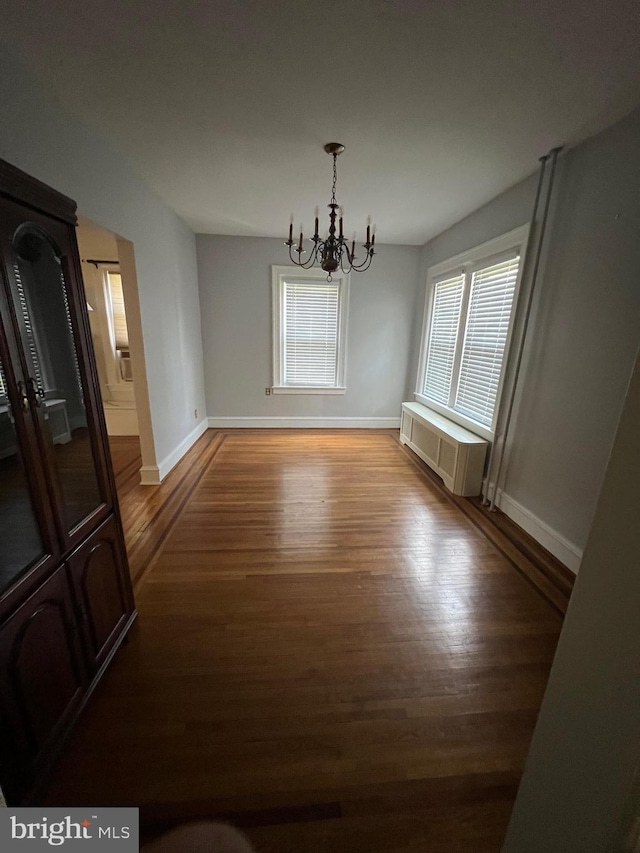 empty room featuring radiator, dark hardwood / wood-style flooring, and a notable chandelier